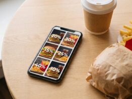 Smartphone mit Coupon-Uebersicht neben einem Fastfood-Menue auf einem Holztisch