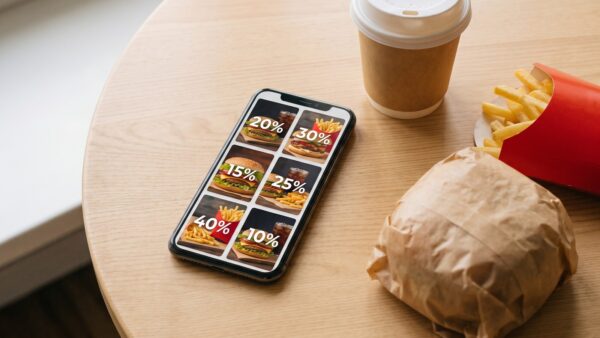 Smartphone mit Coupon-Übersicht neben einem Fastfood-Menü auf einem Holztisch