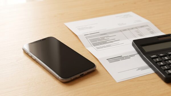 iphone kosten Smartphone neben einer Mobilfunkrechnung und einem Taschenrechner auf einem Holztisch