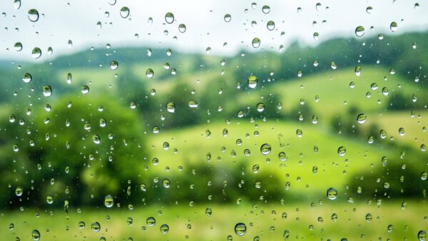 allgaeu outlet fuessen bild 1 Regentropfen auf einer Fensterscheibe vor grüner Landschaft