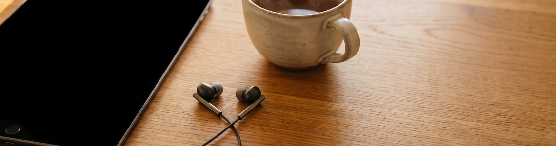 Tablet, Kopfhoerer und Teetasse auf einem hellen Holztisch
