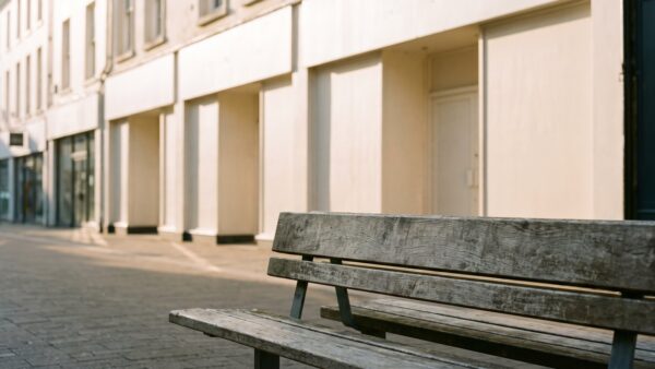 Leere Fußgängerzone mit heller Ladenzeile und Holzbank