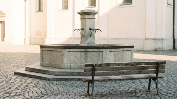 Schlichter Steinbrunnen mit leerer Holzbank davor