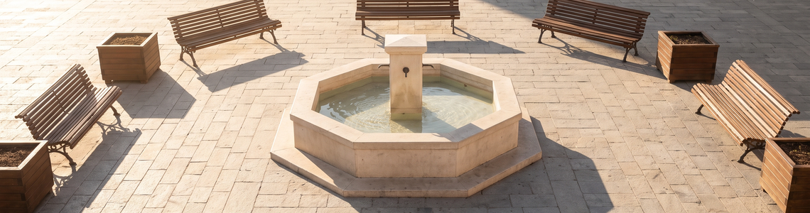 Heller gepflasterter Platz mit Brunnen und leeren Holzbänken