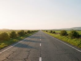Leere Straße durch flaches grünes Land unter hellem Himmel