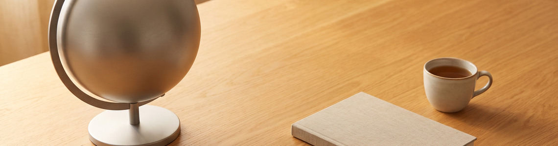 Unbeschrifteter Metallglobus neben Notizbuch und Teetasse
