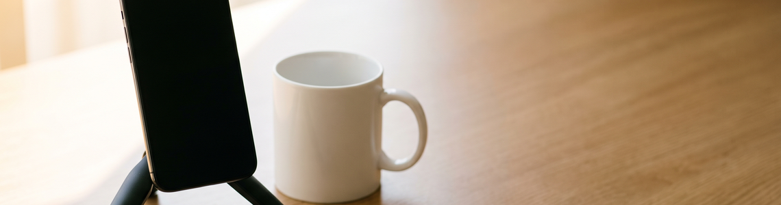 Ausgeschaltetes Smartphone auf einem Stativ neben einer weißen Tasse