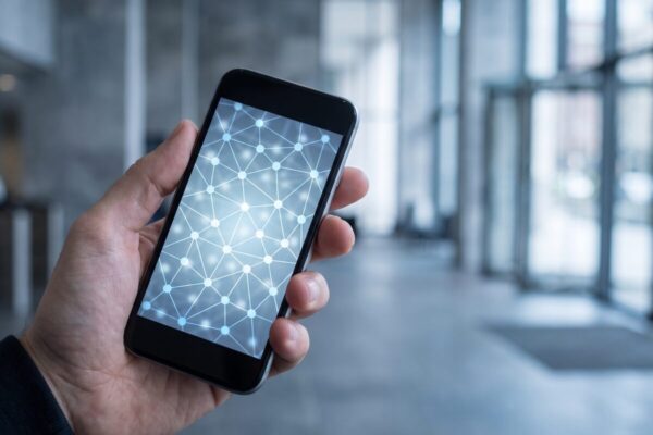 krypto vertrauen hero Hand haelt Smartphone mit leuchtendem Netzwerk aus Knotenpunkten in einer leeren Bankhalle