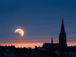 Mondfinsternis 2026 ueber einer Stadtsilhouette in der Morgendaemmerung