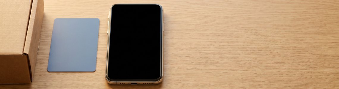 Versandkarton, unbedruckte Karte und Smartphone auf hellem Schreibtisch