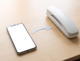 Smartphone mit aktivierter Rufumleitung neben Festnetztelefon auf Schreibtisch
