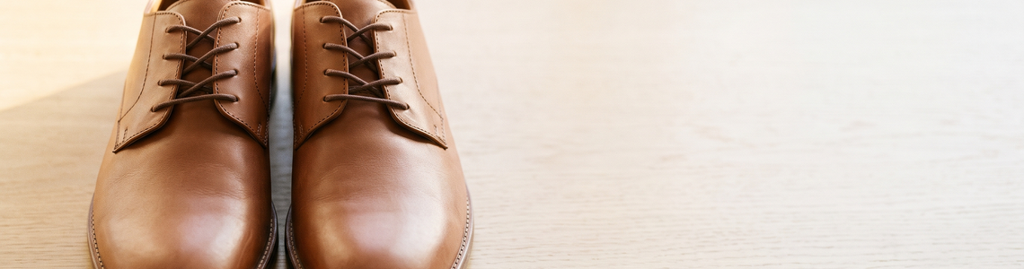Ein Paar schlichte einfarbige Lederschuhe auf einer Holzfläche