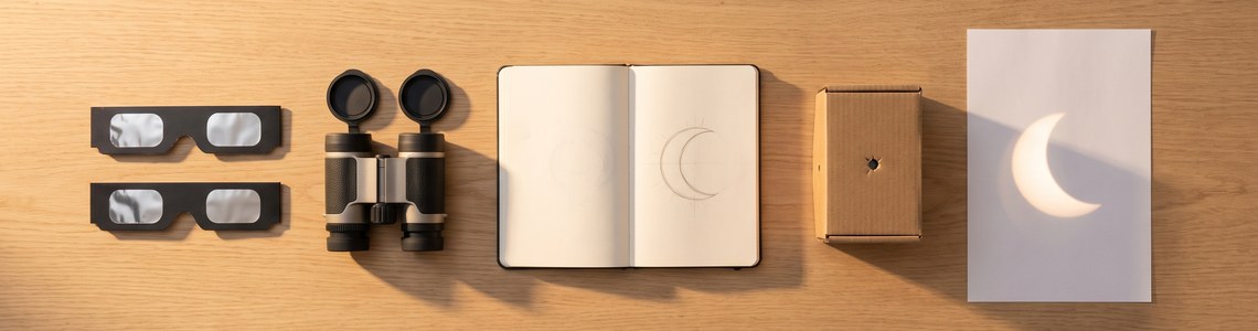 Sonnenfinsternis-Brille, Fernglas und Lochkamera auf einem Holztisch