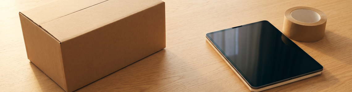 Versandkarton ohne Aufdruck neben Notebook und Packband