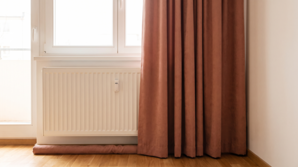 Freistehender Heizkörper am Fenster mit Vorhang und Zugluftstopper