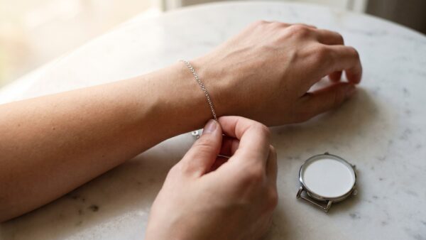 valmano gutschein inline3 Frau legt ein feines Silberarmband an, daneben eine Armbanduhr
