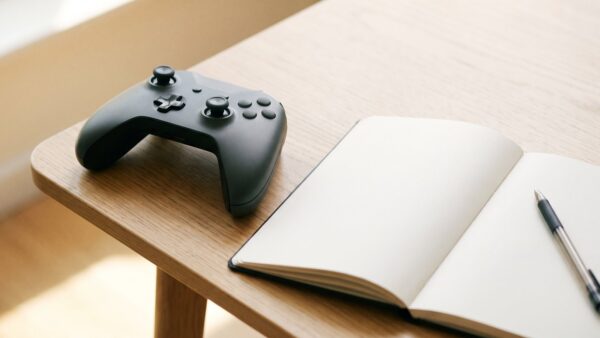 xbox game pass kosten bild 4 Abgelegter Controller neben einem leeren Notizheft auf hellem Holz