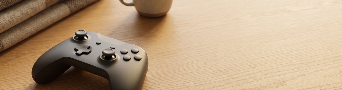 Dunkelgrauer Gaming-Controller mit Decke und Tasse auf hellem Holztisch