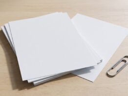 Stapel unbedruckter weißer Blätter mit einem herausgeschobenen Blatt auf heller Holzfläche