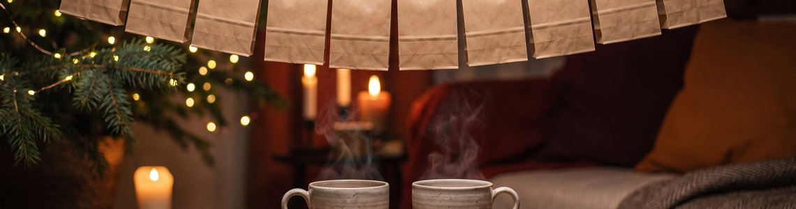 Zwei Teetassen auf einem Holztisch vor einer Leine mit kleinen Papiertüten und einer Lichterkette