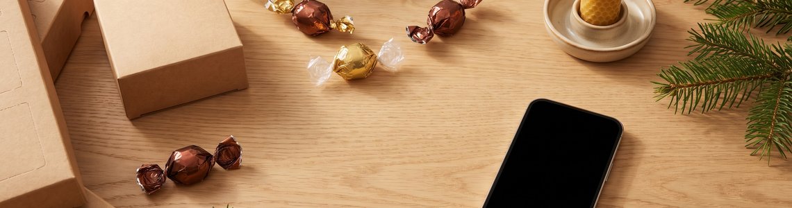 Adventskalender, Pralinen und Smartphone auf hellem Holz
