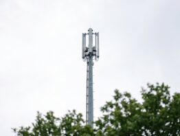 Grauer Mobilfunkmast vor hellem bewölktem Himmel