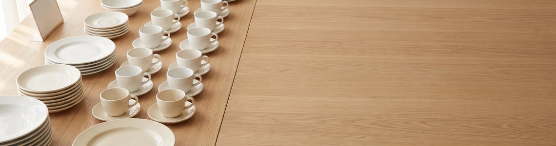 Langer Holztisch mit vielen weißen Tellern und Tassen in Reihen aufgestellt