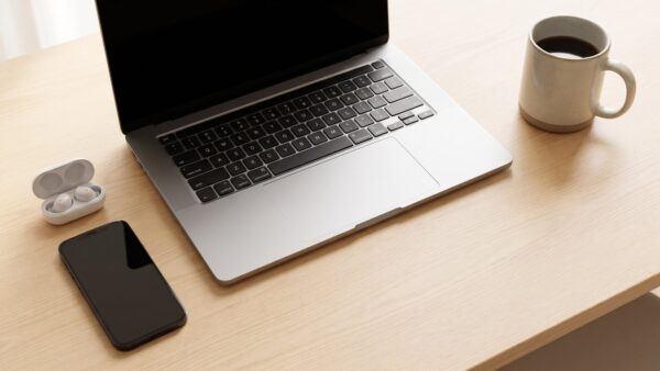 amazon music login bild 1 Laptop, Smartphone mit dunklem Display, Ohrhörer und Kaffeetasse auf einem hellen Schreibtisch