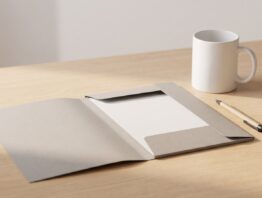 Aufgeklappter leerer Pappordner mit Kugelschreiber und Tasse auf einem Holzschreibtisch