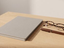 Geschlossener unbeschrifteter Aktendeckel mit Lesebrille und Füller auf einem hellen Schreibtisch