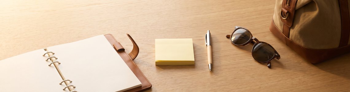 Taschenkalender, Haftnotizen und Reisetasche auf einem Schreibtisch