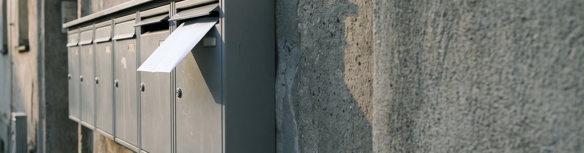 Weißer Briefumschlag ragt aus einem grauen Hausbriefkasten heraus