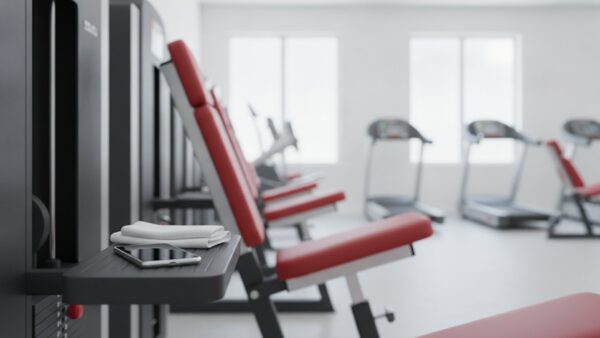clever fit login bild 3 Kraftgeräte mit roten Polstern in einer hellen Trainingsfläche, auf der Ablage ein Smartphone und ein Handtuch