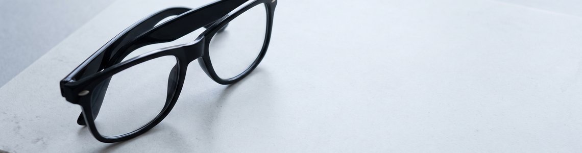 Schlichte schwarze Brille mit kräftigem Rahmen auf einer hellen Steinplatte