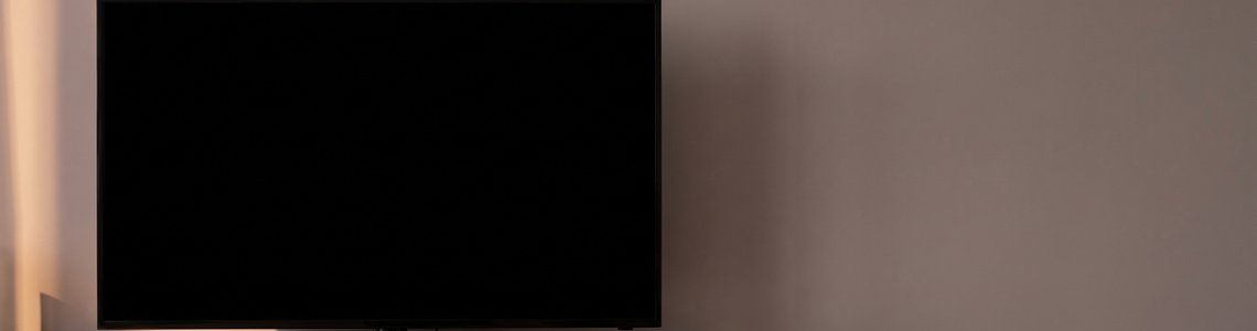 Dunkler Fernsehbildschirm im Wohnzimmer mit Fernbedienung und Smartphone auf dem Sideboard