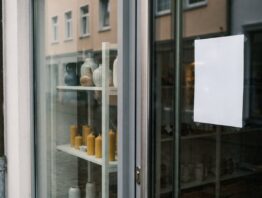 Schaufenster eines Deko-Geschäfts mit wenigen Vasen und Kerzen und einem leeren Aushang an der Tür