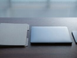 Unbeschrifteter Aktenordner neben einem zugeklappten Laptop und einem Smartphone auf einem Holztisch