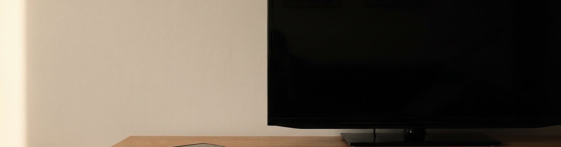 Ausgeschalteter Fernseher auf einem Sideboard, daneben ein Smartphone mit dunklem Display