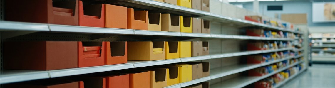 Süßwarenregal im Supermarkt mit mehreren leeren Fächern zwischen neutralen Kartons
