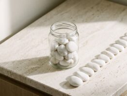 Glasgefäß mit weißen Kieselsteinen und eine Reihe einzeln abgelegter Steine daneben