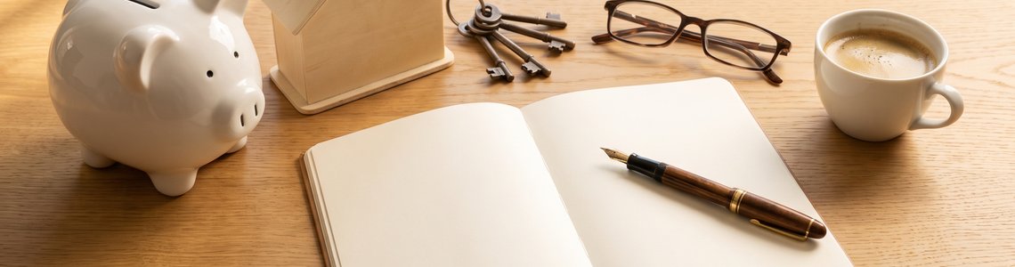 EZB Leitzins: Sparschwein, Hausmodell und Notizbuch auf dem Schreibtisch