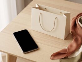 Smartphone mit leerem Bildschirm neben einer unbedruckten Einkaufstasche, einem Seidenschal und einer Schmuckschachtel
