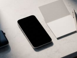 ghost pairing bild 1 Smartphone mit schwarzem Display neben einer leeren Notizkarte, ein zweites Gerät liegt im Schatten am Bildrand