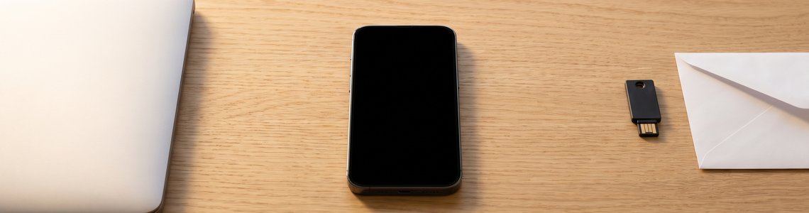Laptop, ausgeschaltetes Smartphone, Sicherheitsschlüssel und leerer Briefumschlag auf einem Holzschreibtisch