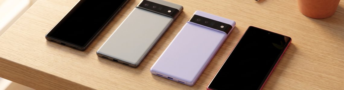 Vier Smartphones in Schwarz, Grau, Lavendel und Beerenrot nebeneinander auf einem Holzschreibtisch