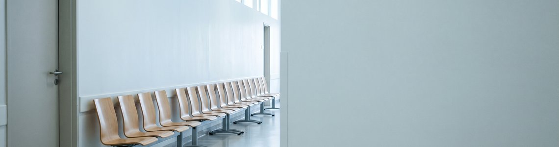 Leere Wartestühle in einem hellen Amtsflur mit geschlossener Tür