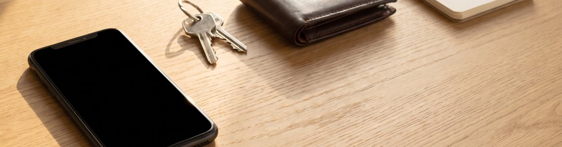 Smartphone mit schwarzem Display neben Schlüsselbund und Brieftasche auf einem Holzschreibtisch