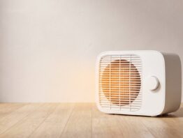 Weißer Keramik-Heizlüfter mit warm leuchtendem Lüftungsgitter auf einem Holzboden