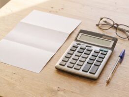Leerer Briefbogen, Taschenrechner mit leerem Display und Lesebrille auf hellem Holztisch