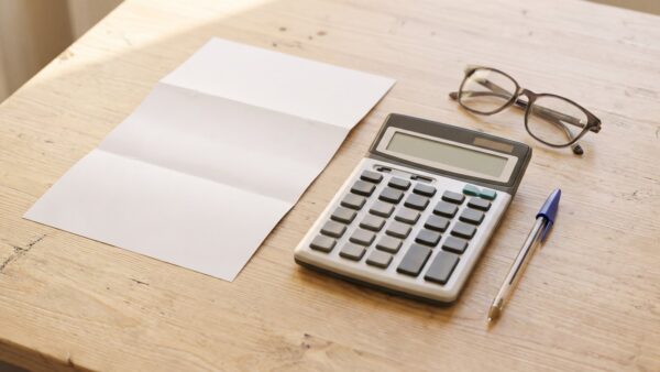 Leerer Briefbogen, Taschenrechner mit leerem Display und Lesebrille auf hellem Holztisch
